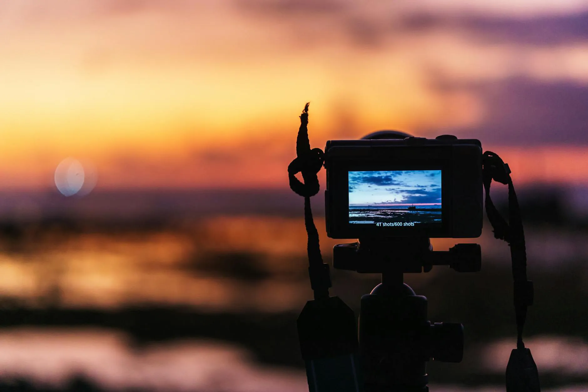 A camera on a tripod captures the vibrant colors of a sunset over water.
