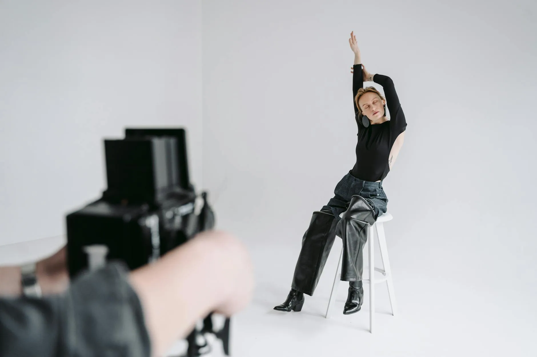 A woman poses elegantly on a stool in a bright studio, captured during a photoshoot.