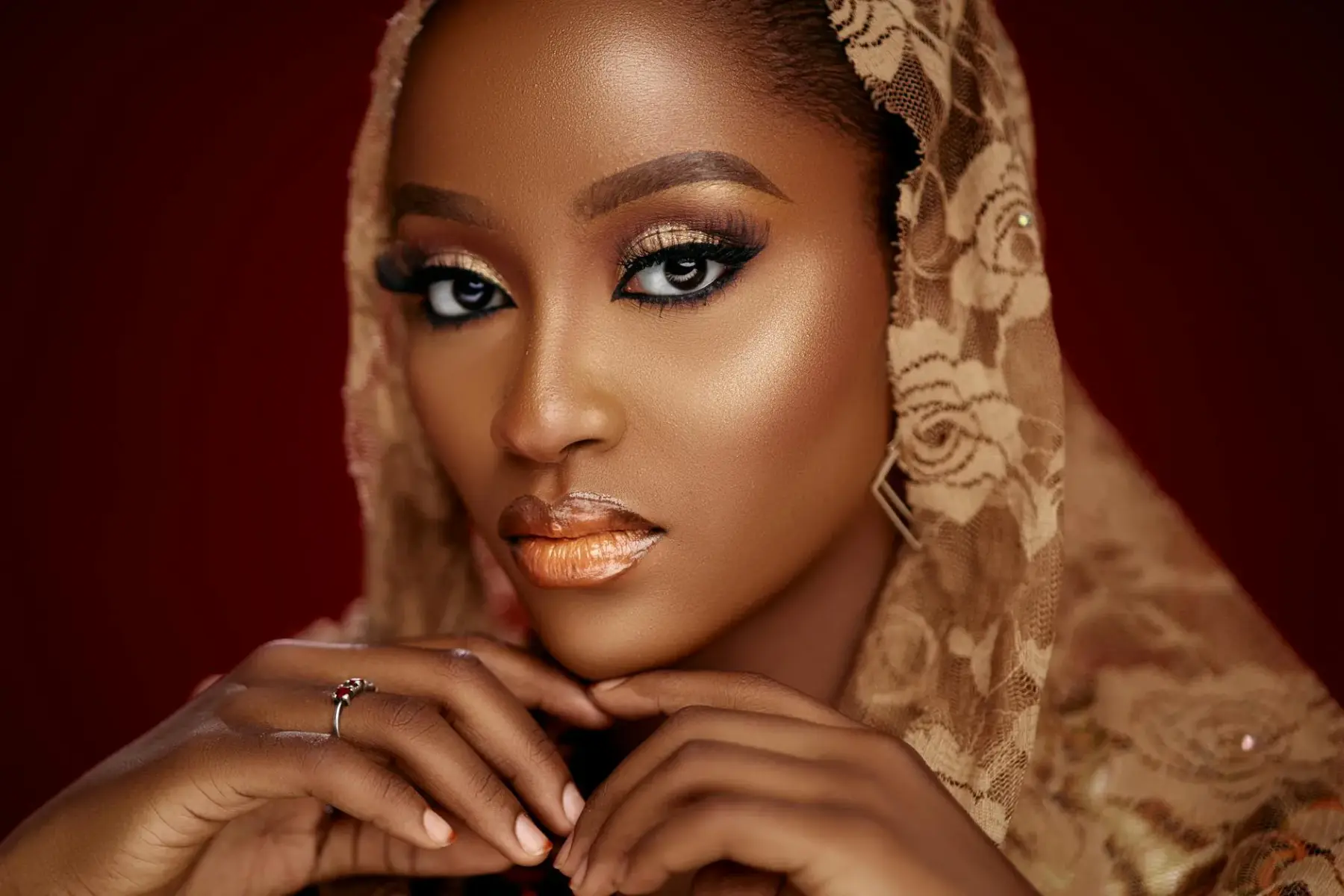 Striking headshot of a woman with beautiful makeup and lace shawl set against a dark background.