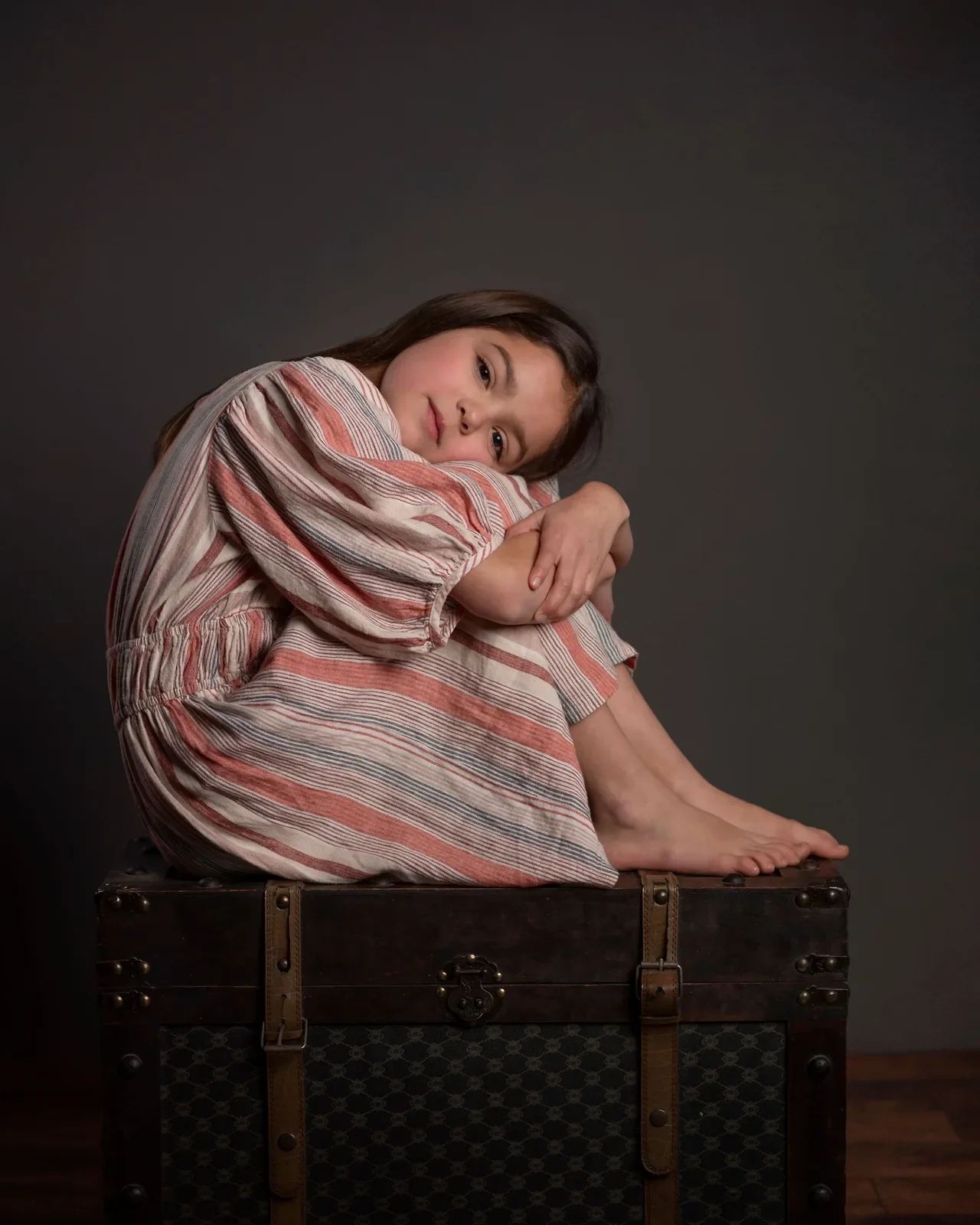 Dziewczynka w pasiastej sukience na starym kufrze w studio fotograficznym
